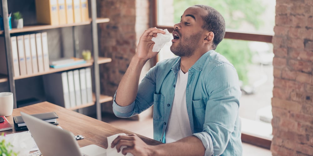 Man sneezing at computer